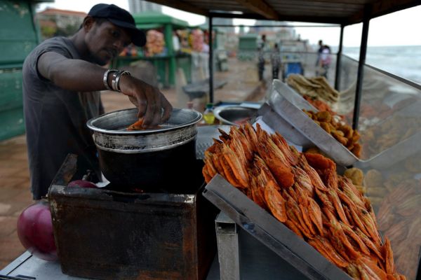 A street food vendor is prepareing a local delicacy to be offered to a customer during a colombo street food tour