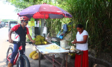 cycle rider near a lady who cutting jack fruits